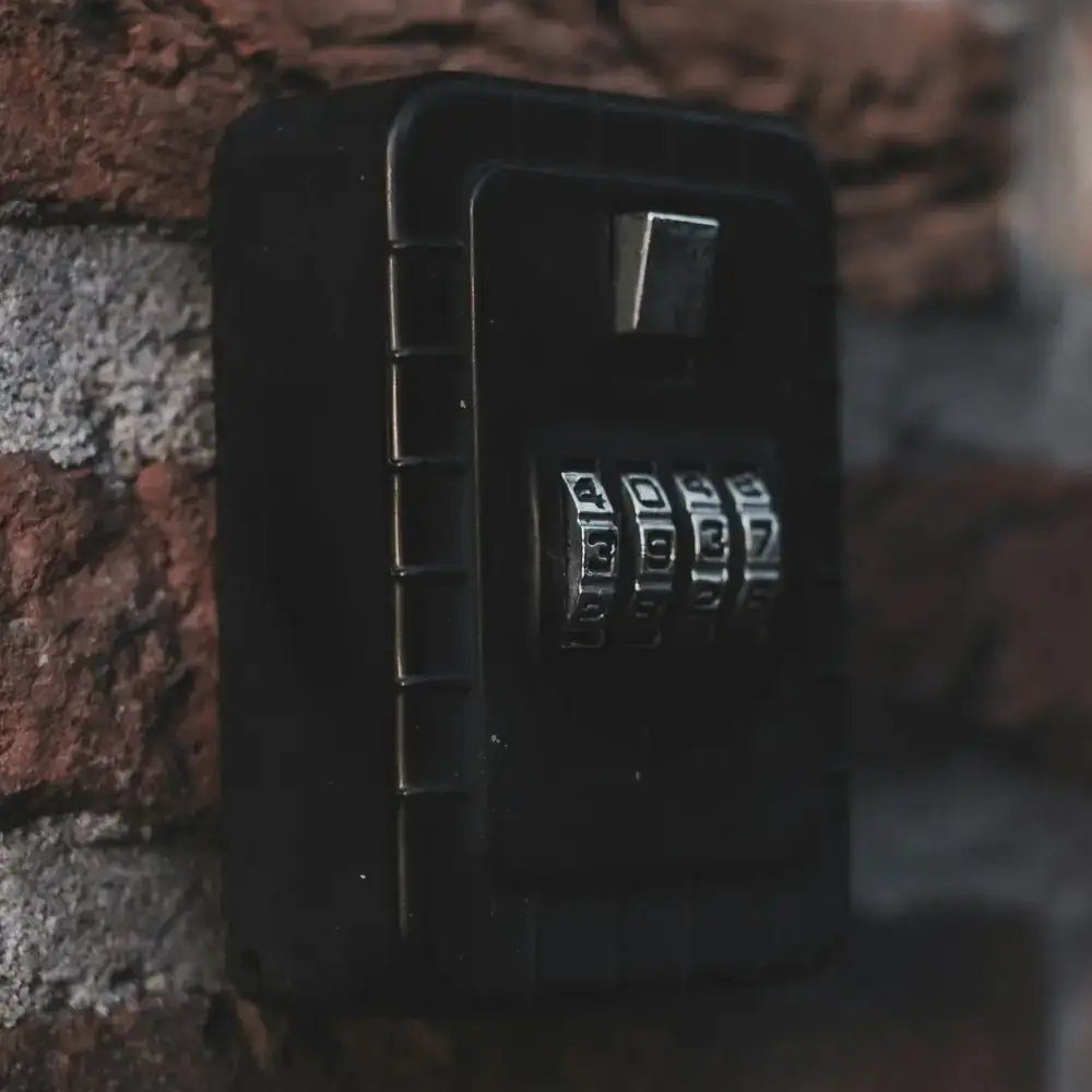 A black combination key lockbox mounted on a brick wall